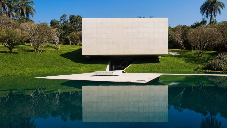 Galeria Adriana Varejão no Instituto Inhotim, com arquitetura contemporânea de concreto refletida em um espelho d'água, cercada por jardins.